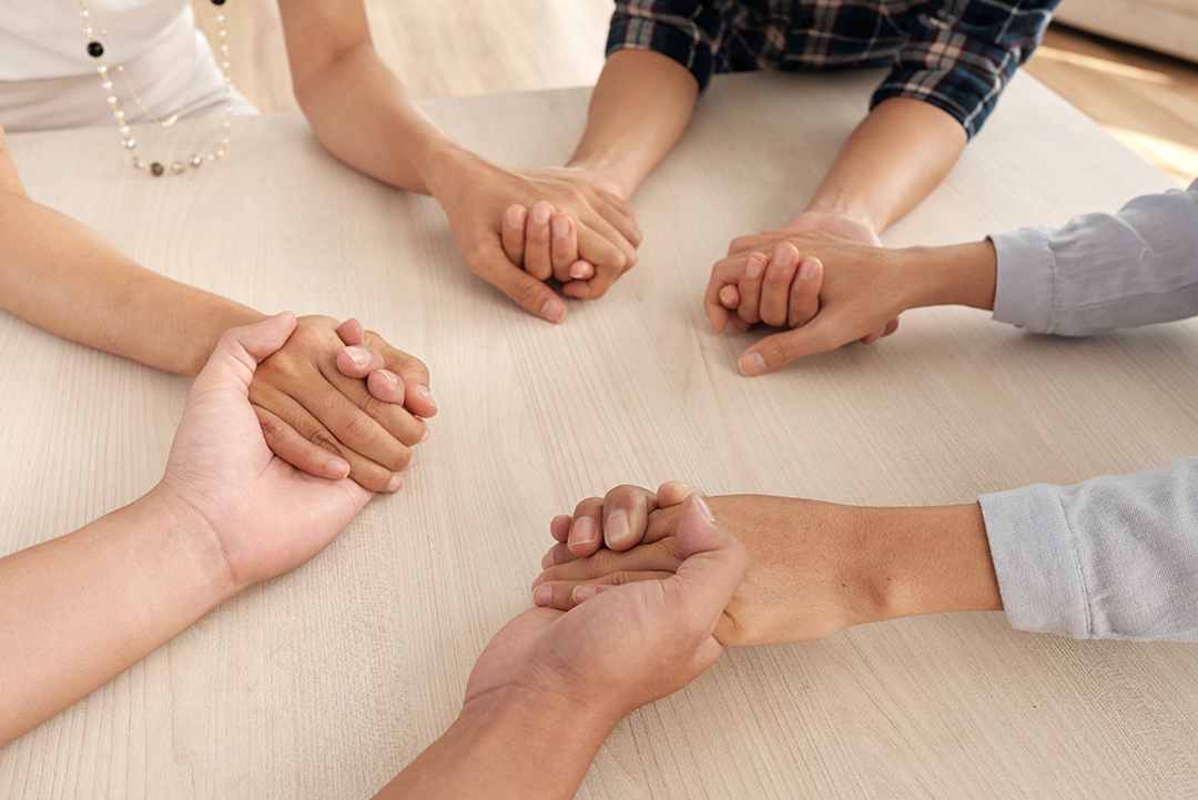 four-unrecognizable-people-sitting-around-table-holding-each-other-s-hands-middle.jpg